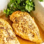 Close up of baked lemon chicken in a white rectangular casserole dish with parsley to the side for garnish and a text overlay on the photo.