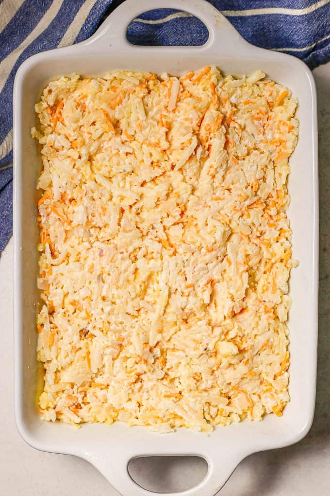 A hash brown casserole in a large white rectangular casserole dish before being cooked.