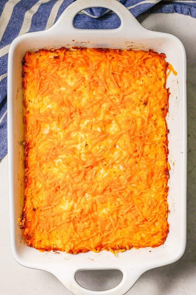 Baked cheesy hash brown casserole in a large rectangular white baking dish.