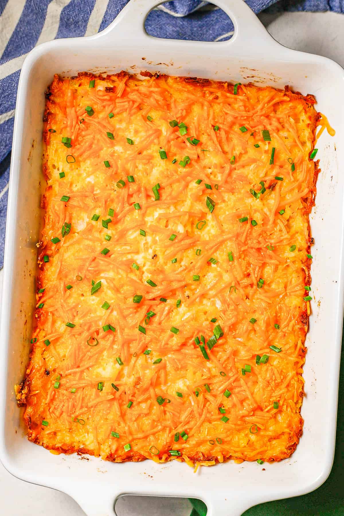 Baked cheesy hash brown casserole in a large rectangular white baking dish with sliced green onions sprinkled on top.