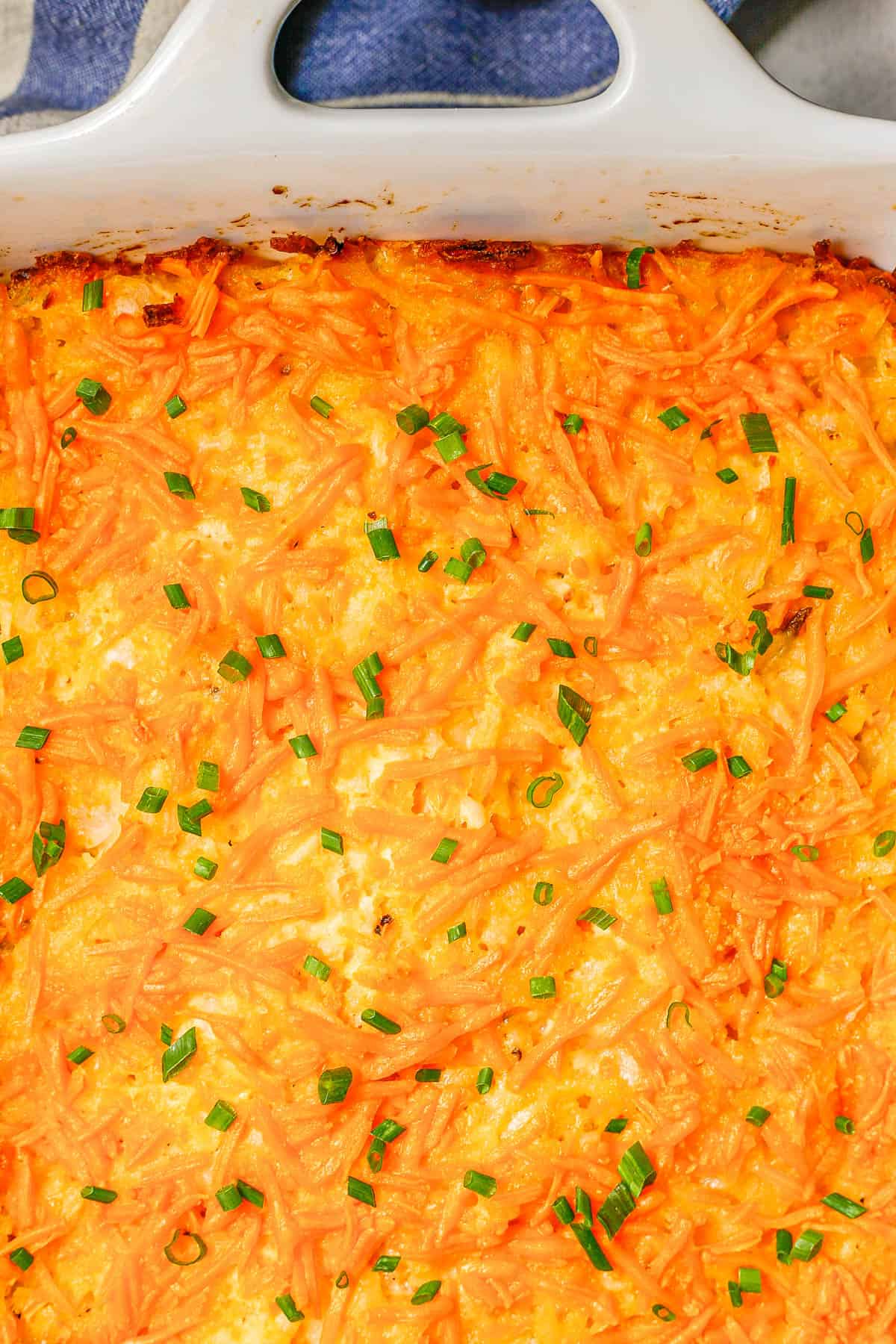 Close up of a baked cheesy hash brown casserole in a large rectangular white baking dish.