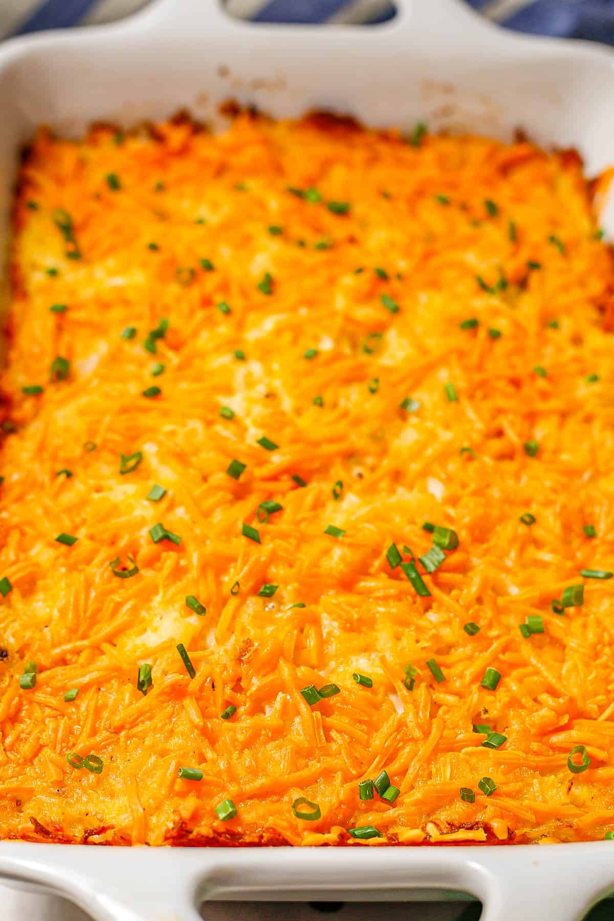 A side angle of baked cheesy hash brown casserole in a white rectangular casserole dish.