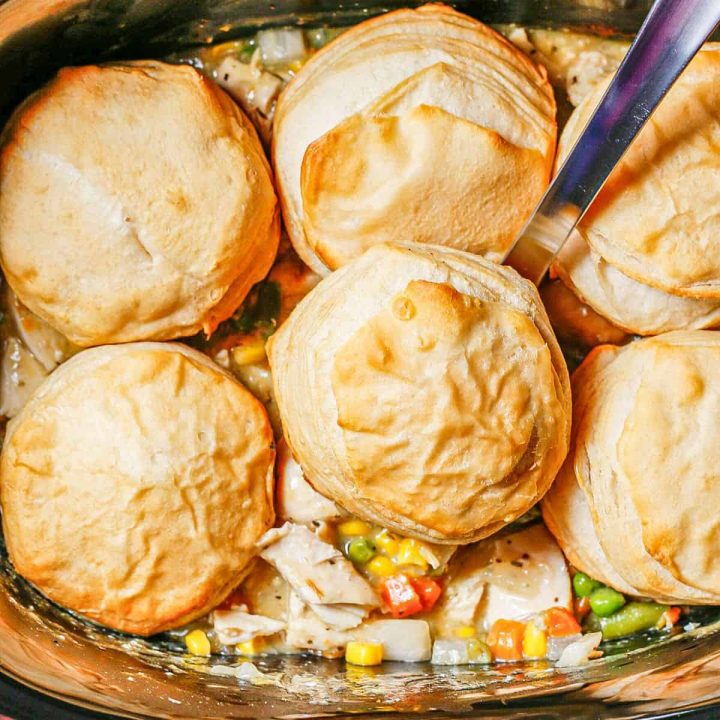 Close up of a silver ladle scooping up chicken pot pie and a biscuit from a slow cooker.