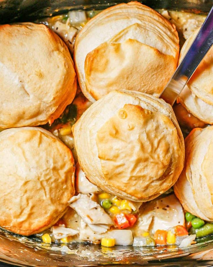 Close up of a silver ladle scooping up chicken pot pie and a biscuit from a slow cooker.