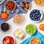 A collection of tiny containers with different colorful healthy kids snacks on a counter with a text overlay on top.