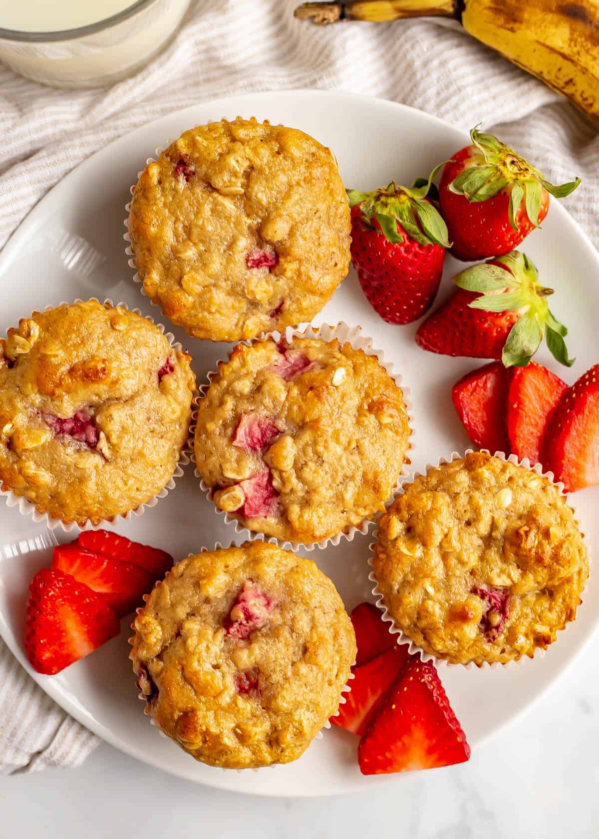 Close up of healthy strawberry banana muffins served on a white plate with sliced and whole strawberries.