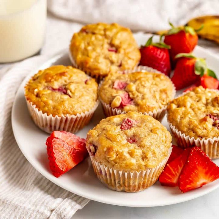 Healthy strawberry banana muffins served on a white plate with sliced and whole strawberries.