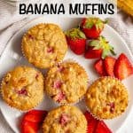 Strawberry banana muffins on a white plate with sliced strawberries on the plate and a glass of milk nearby and a text overlay on the photo.