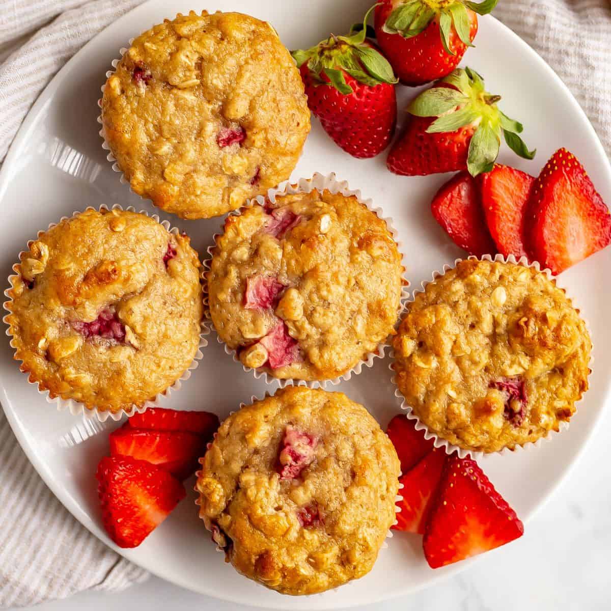 Close up of baked healthy strawberry banana muffins served on a white plate with sliced and whole strawberries.