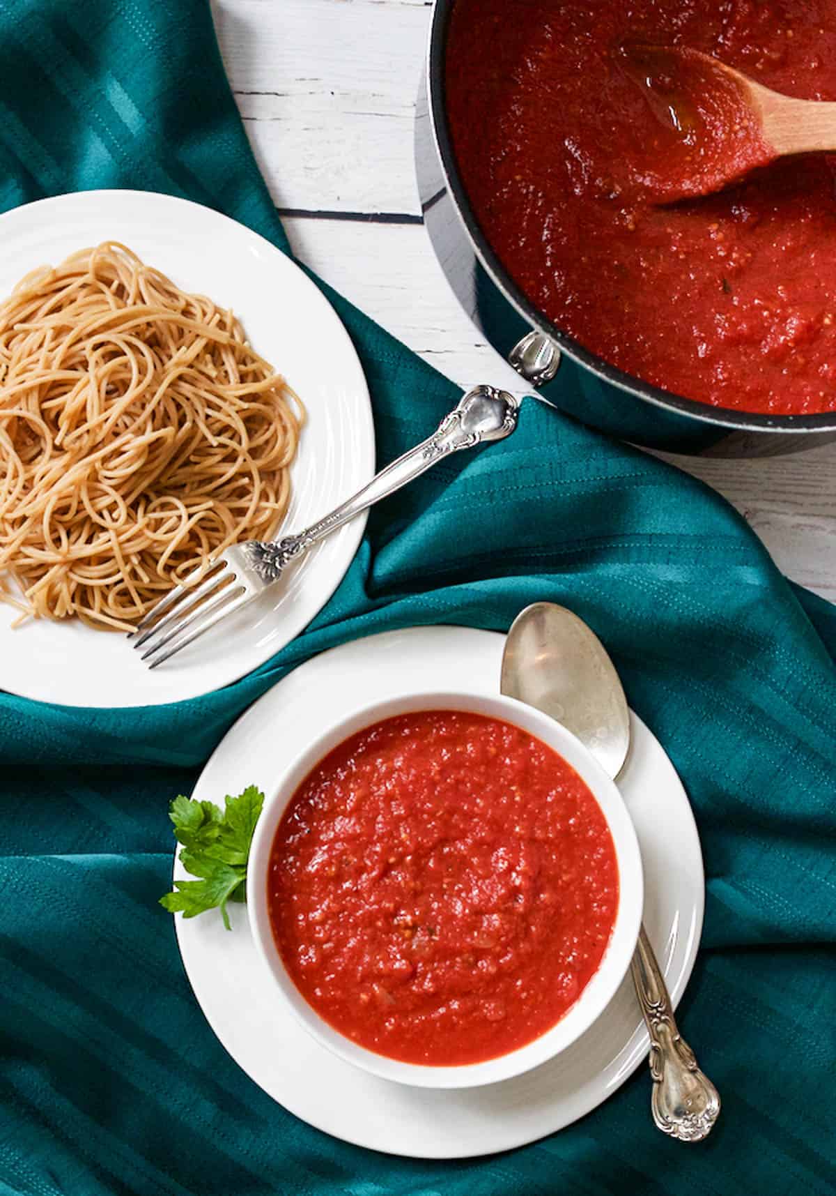 A bowl full of homemade spaghetti sauce with the pot in the background and a bowl of spaghetti noodles to the side.