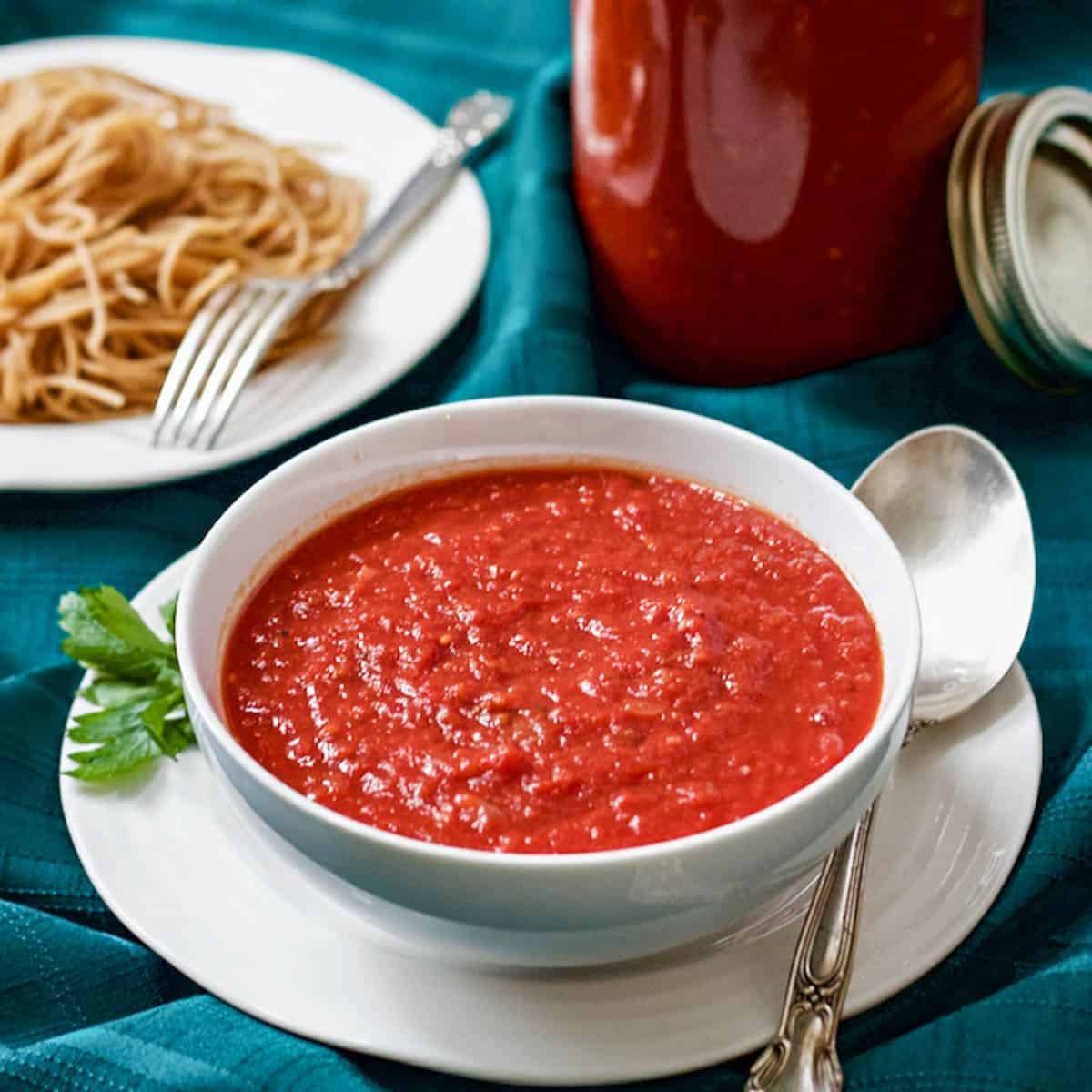 Close up of homemade spaghetti sauce in a white bowl with a jar of extra sauce in the background a bowl of spaghetti noodles to the side.