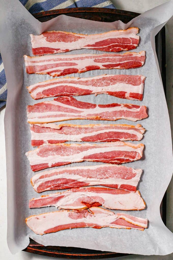 Raw bacon laid out on a parchment paper lined baking sheet.