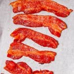 Strips of cooked bacon on a parchment paper lined baking sheet with a text overlay on the photo.