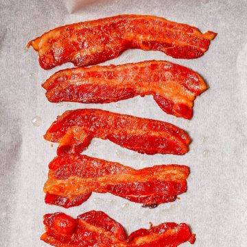 Close up of cooked oven bacon strips on a parchment paper lined baking sheet.