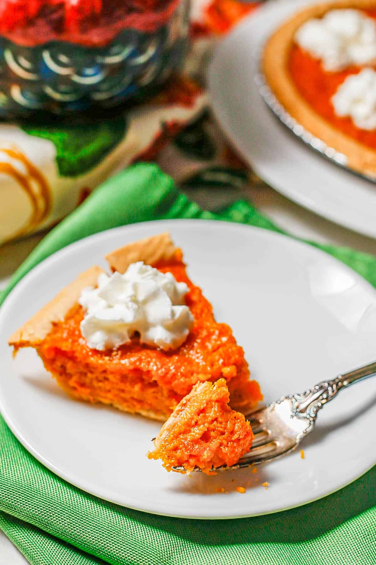 A fork holding a forkful of sweet potato pie on a small white plate.