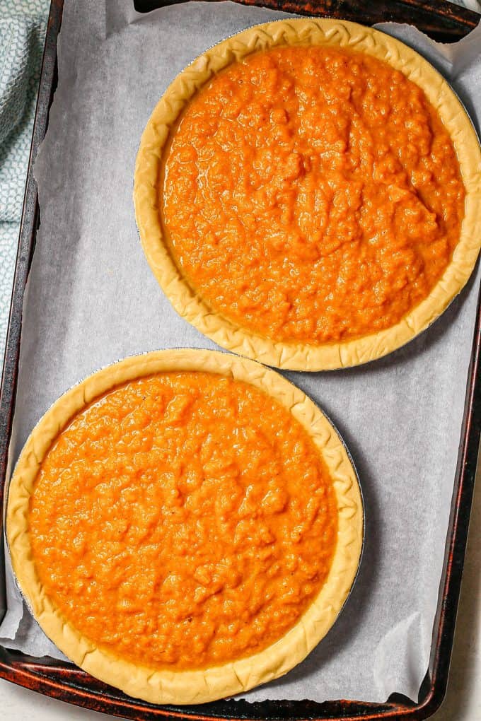 Two pie crusts filled with sweet potato pie on a large baking sheet.