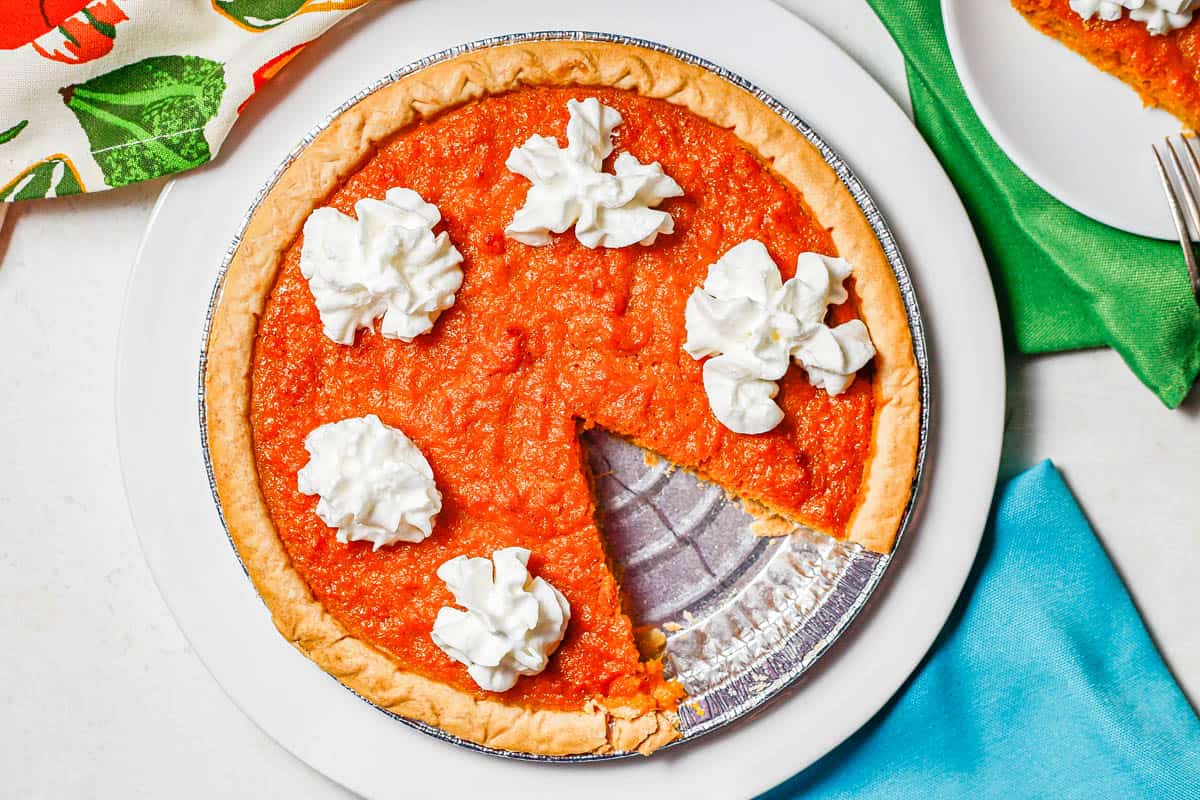 Sweet potato pie served with whipped cream and a slice taken out.