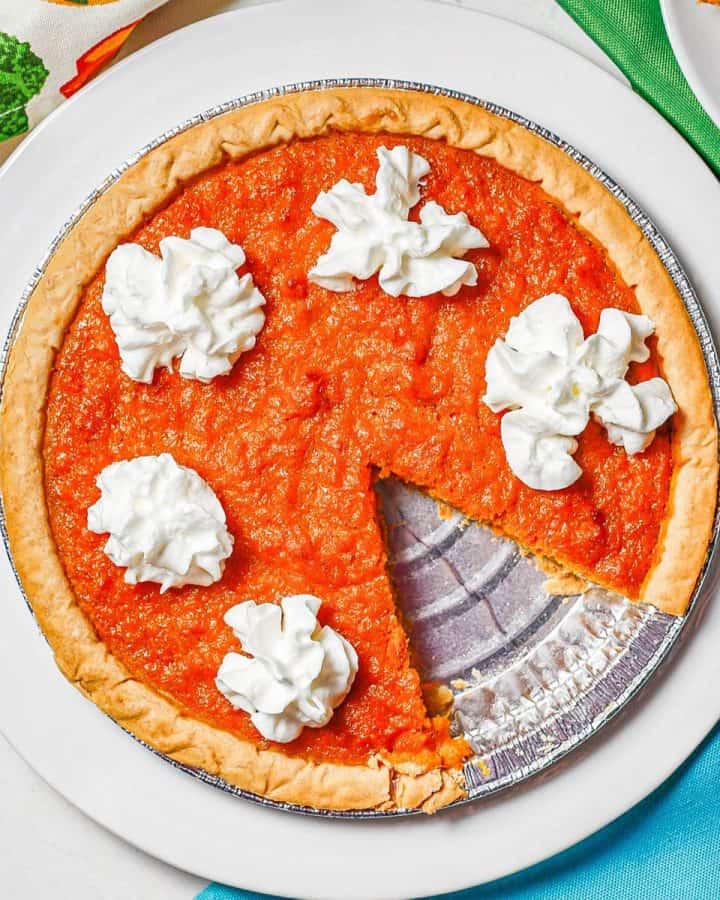 Close up of a sweet potato pie with whipped cream on a white serving plate.