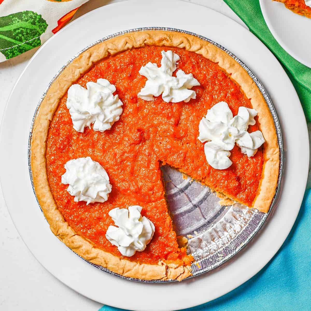 Close up of a sweet potato pie with whipped cream on a white serving plate.