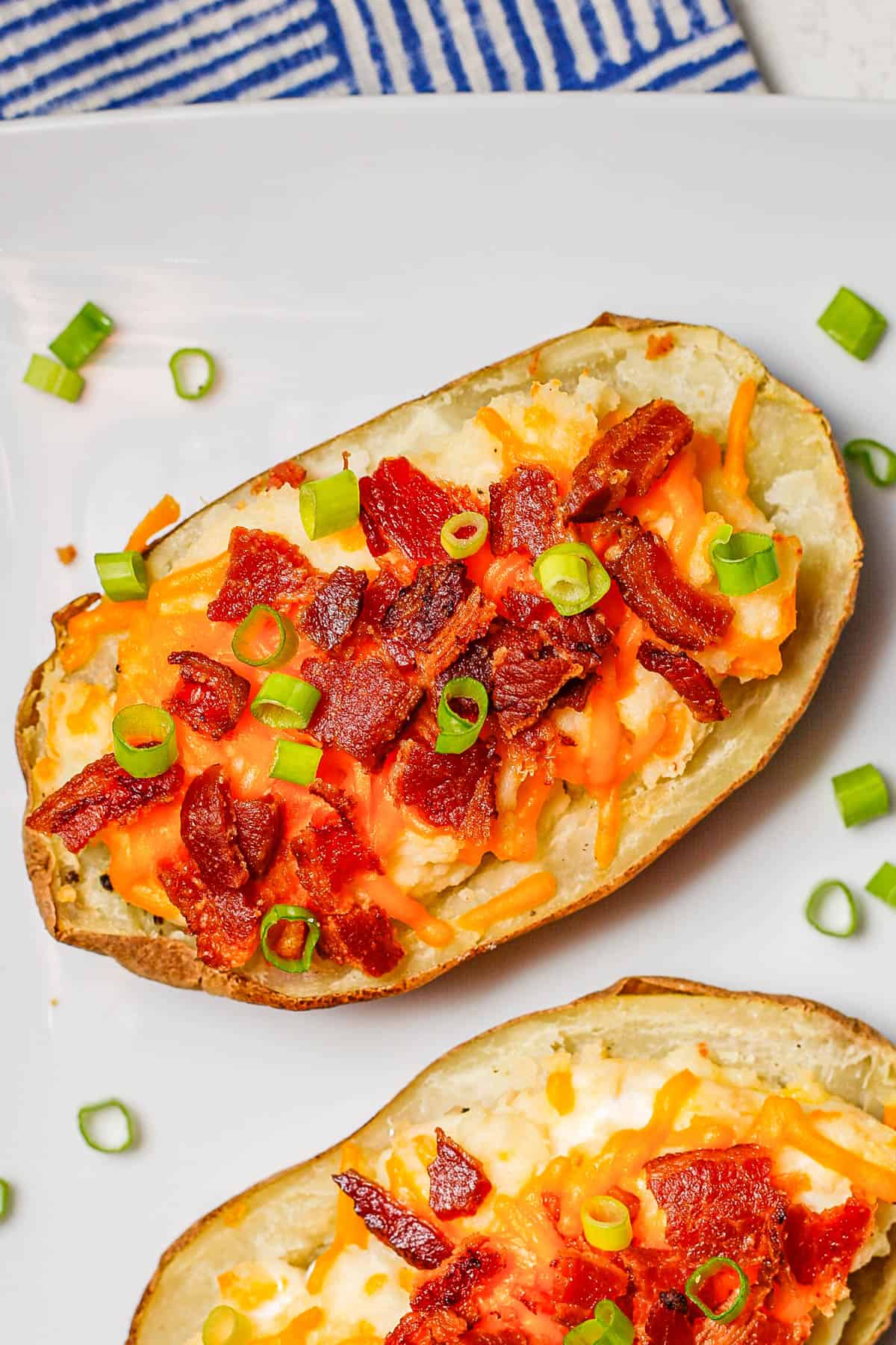 Loaded potatoes with cheese, bacon and green onions on a white serving platter.