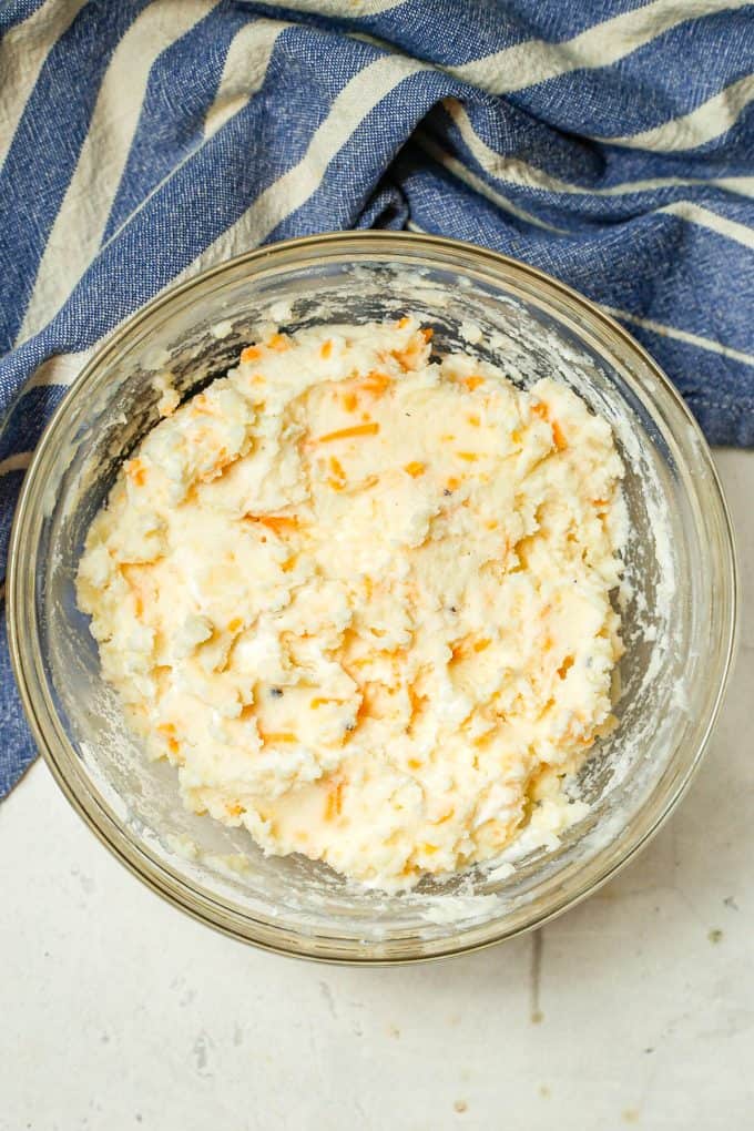 Potatoes mashed with cheese, sour cream and milk in a large glass bowl.