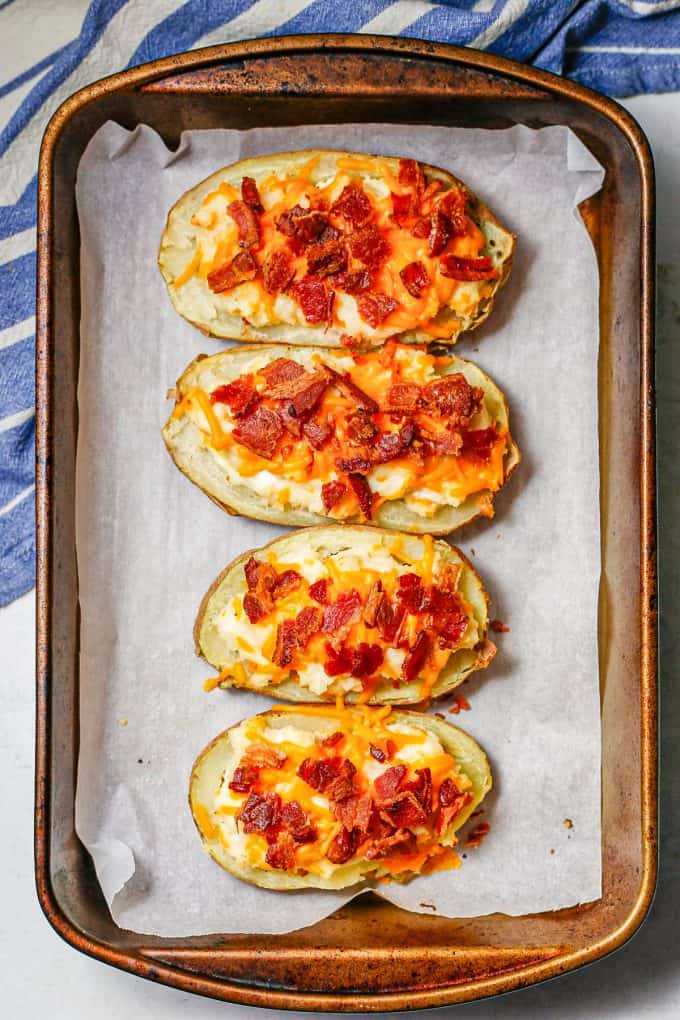 Twice baked potatoes in a baking pan with cheese and bacon on top.