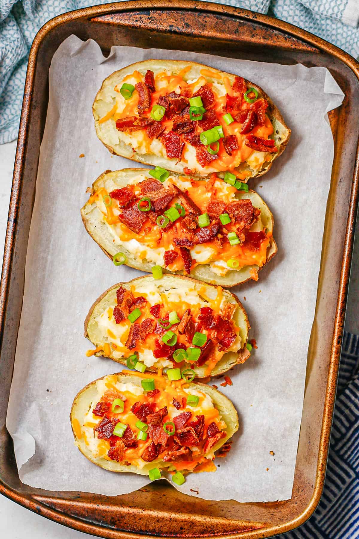 Loaded twice baked potatoes after baking on a baking sheet with sliced green onions on top.