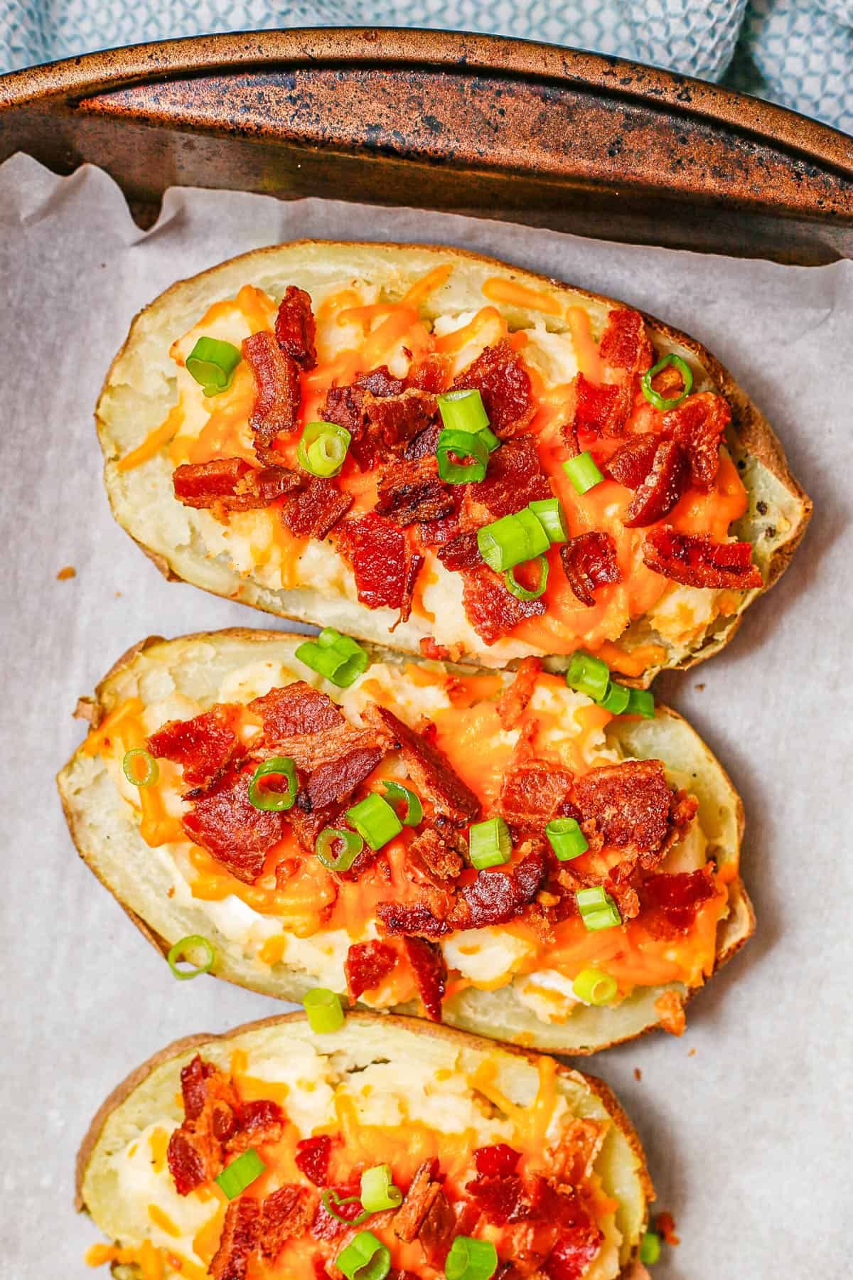 Close up of twice baked potatoes on a baking sheet with green onions on top.