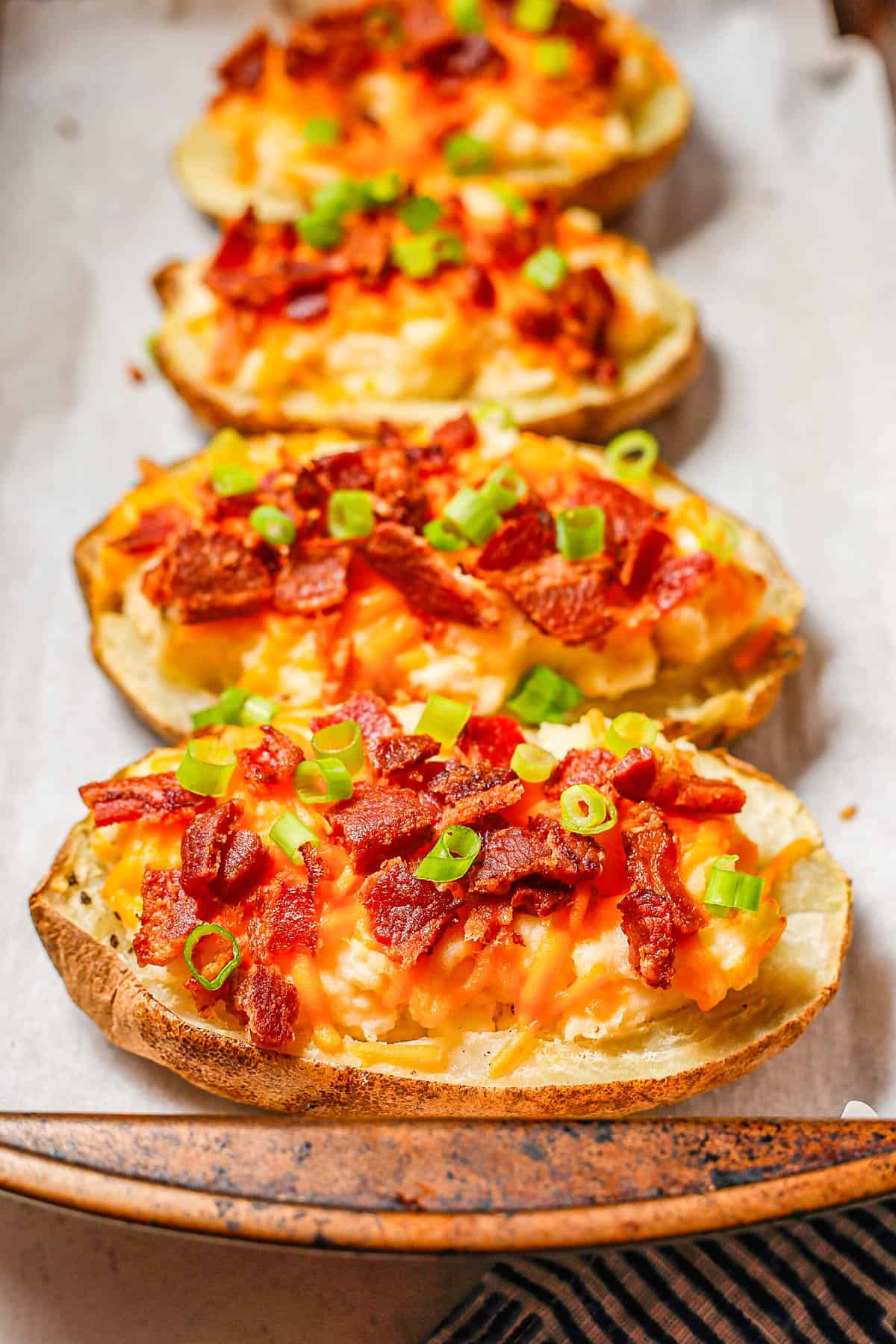 Close up of loaded twice baked potatoes on a parchment paper lined baking sheet with sliced green onions on top.