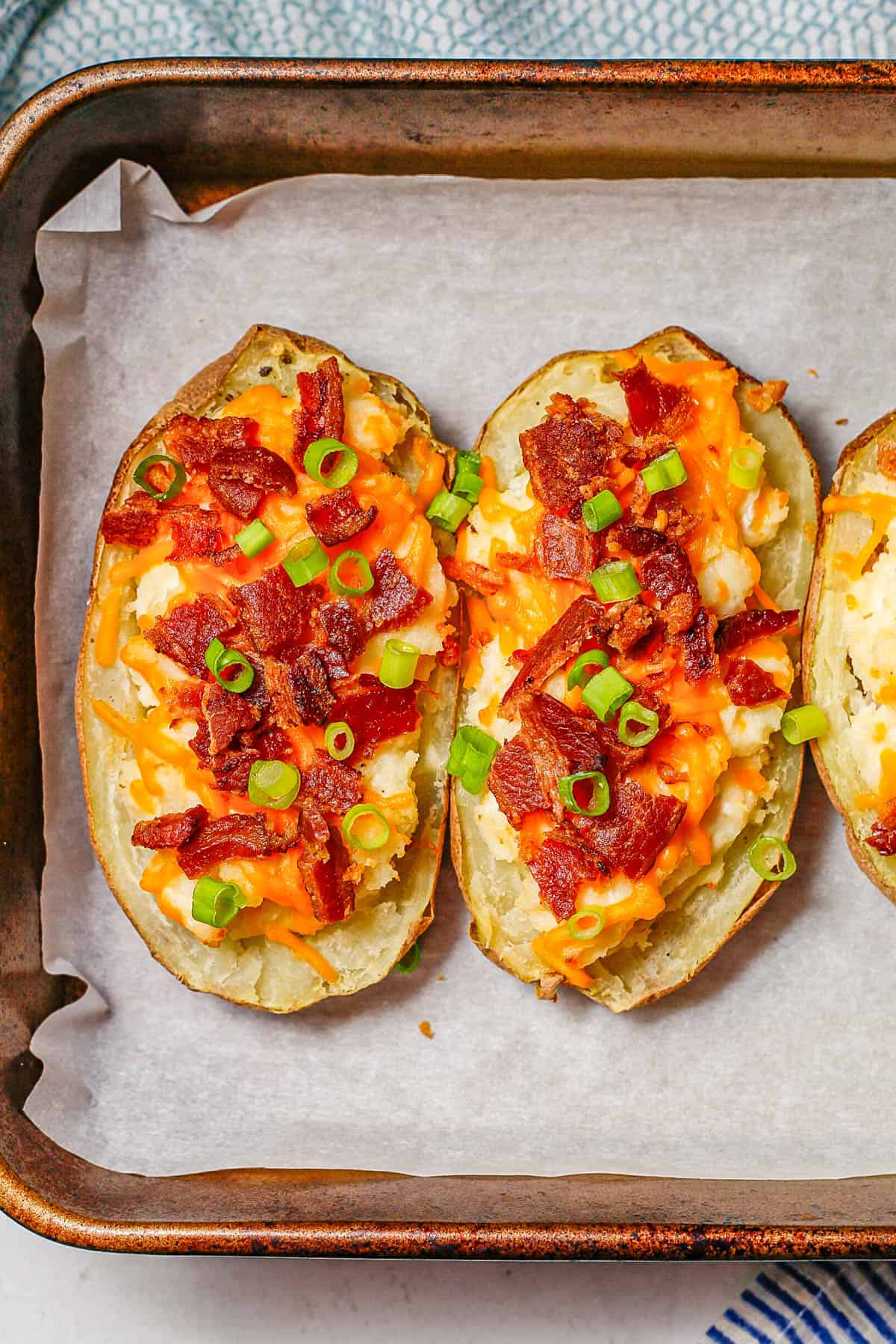 Cheese and bacon topped twice baked potatoes on a parchment paper lined baking pan.
