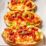 Close up of loaded twice baked potatoes on a parchment paper lined baking sheet with sliced green onions on top and a text overlay on the photo.