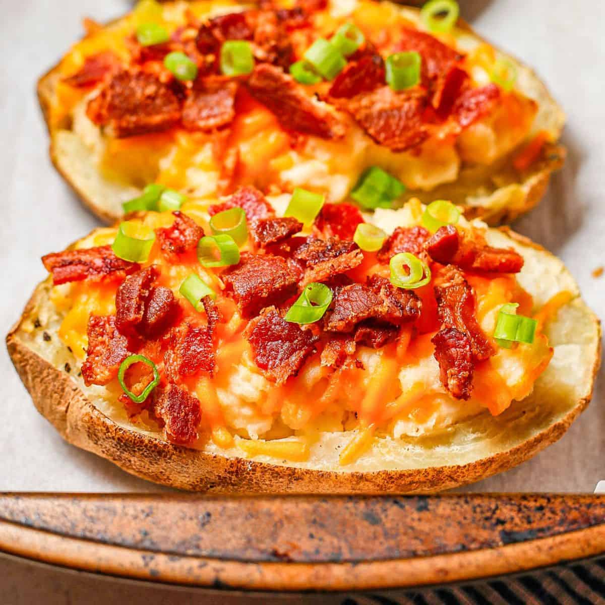 Cropped close up of loaded twice baked potatoes on a parchment paper lined baking sheet with sliced green onions on top.