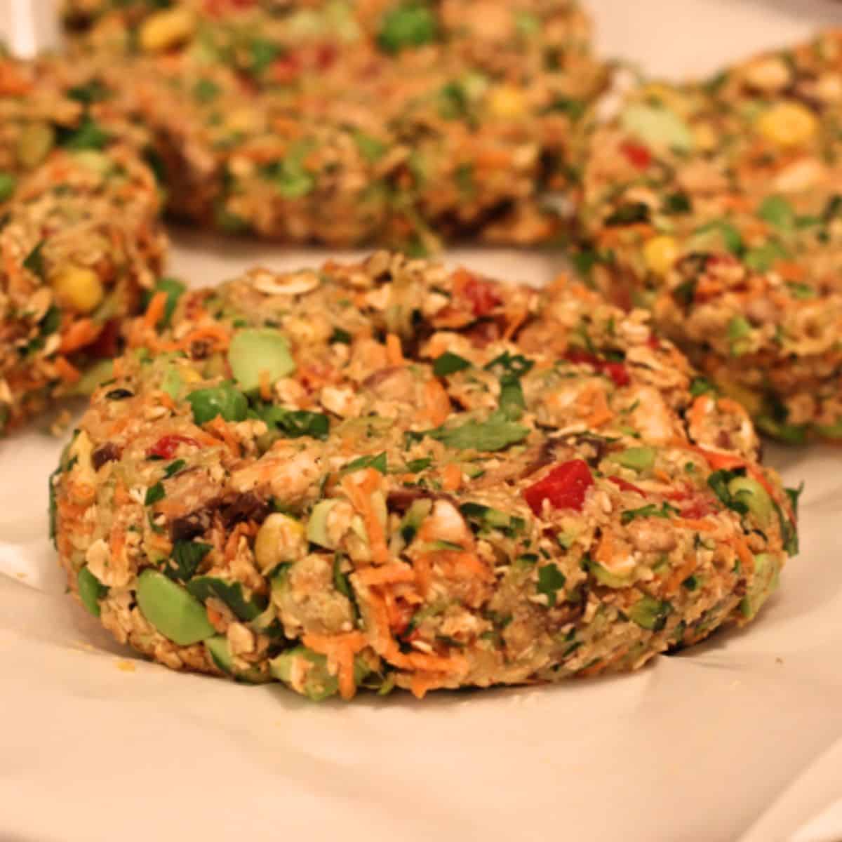 Close up of a veggie loaded veggie burger shaped and resting on a parchment paper lined plate before being cooked.