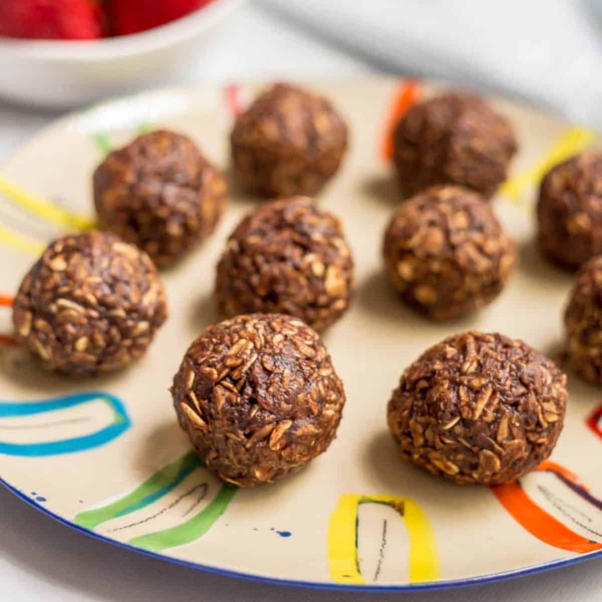 Close up of round chocolate oat cookie balls lined up on a red colorful plate.