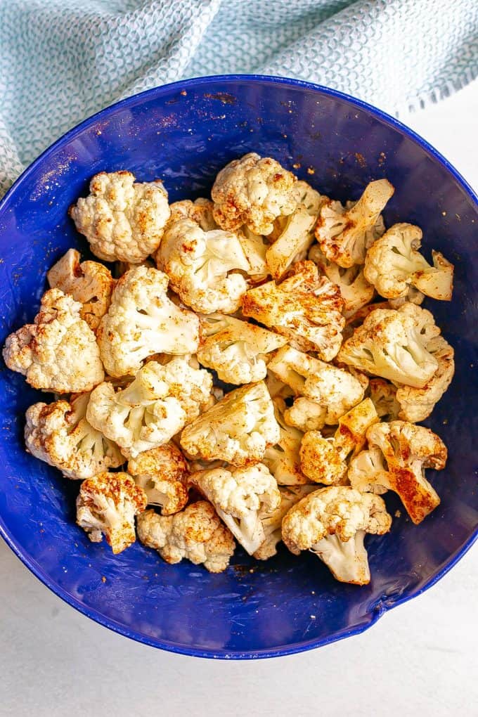 A blue bowl with raw cauliflower florets tossed in a seasoning mix.