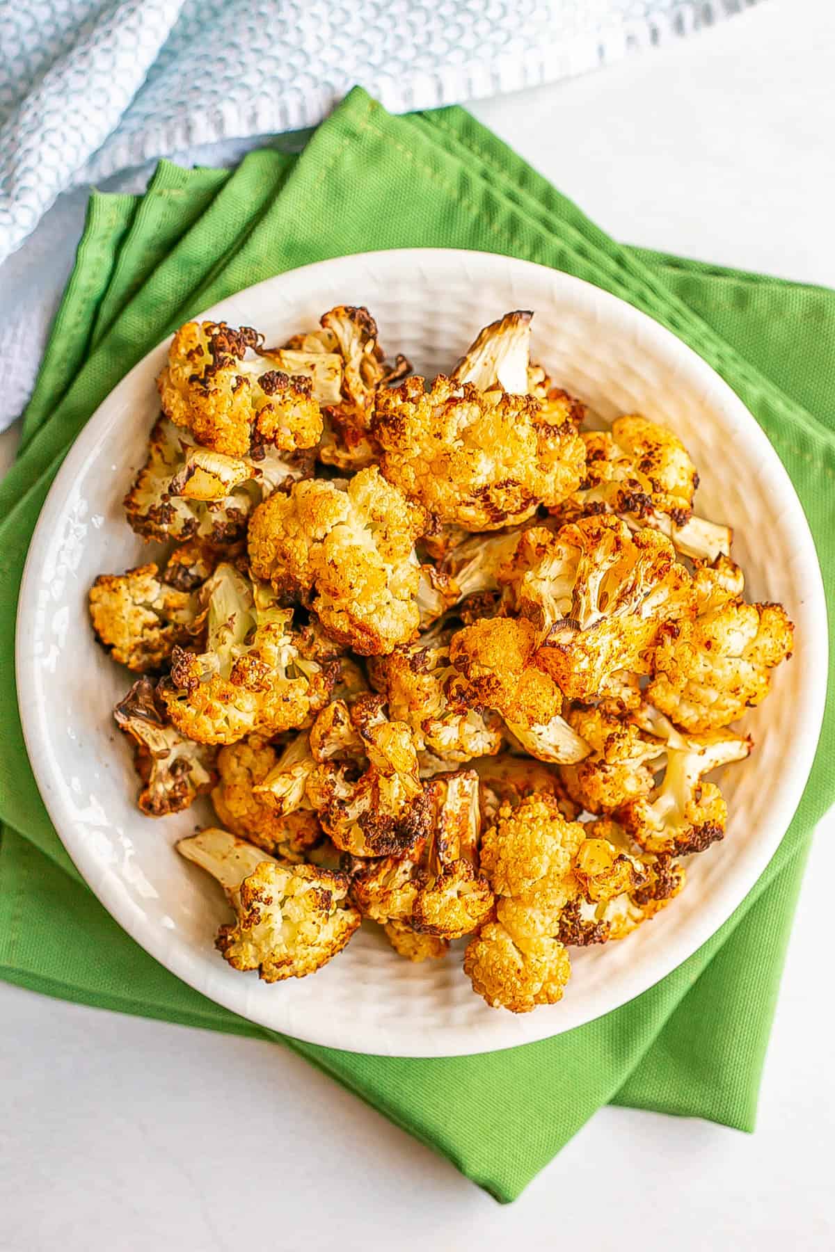 A white bowl of cooked cauliflower florets set on green napkins.