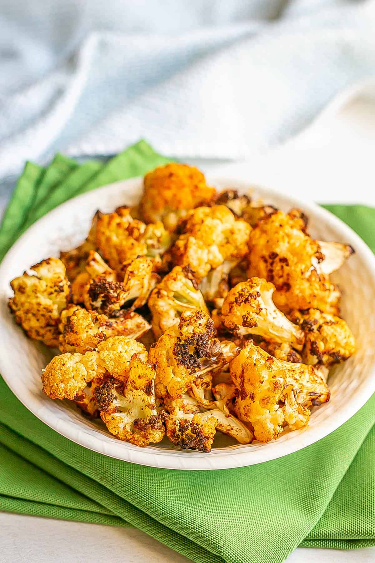 Crispy browned cauliflower florets in a white bowl set on green napkins.