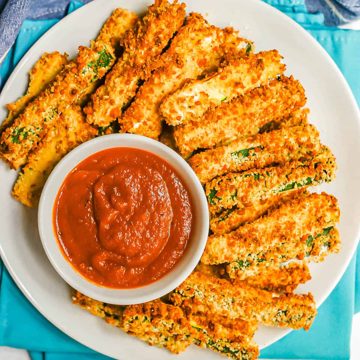 Close up of a plate of zucchini fries on a round white plate with a small bowl of marinara.