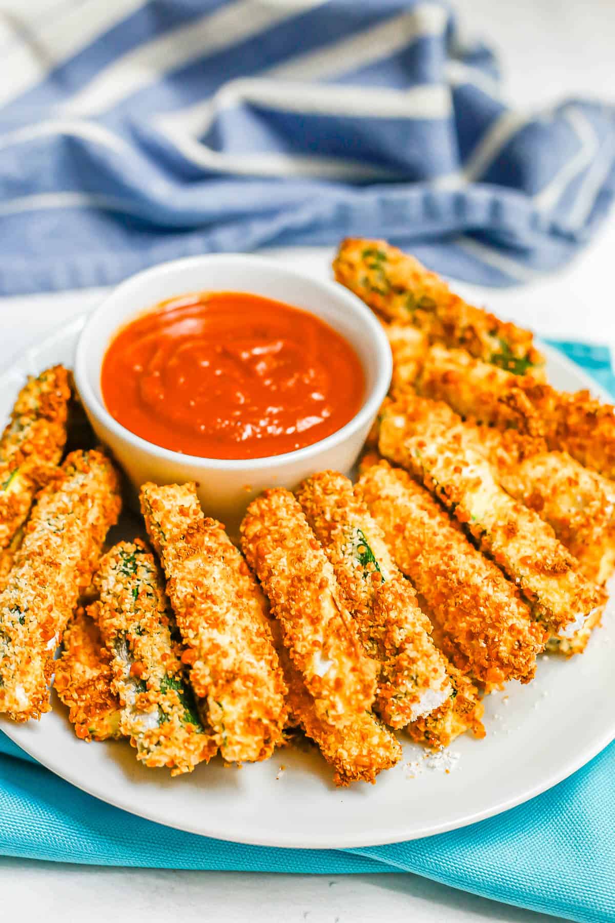 Air Fryer zucchini fries served on a round white plate with a small bowl of marinara for dipping.