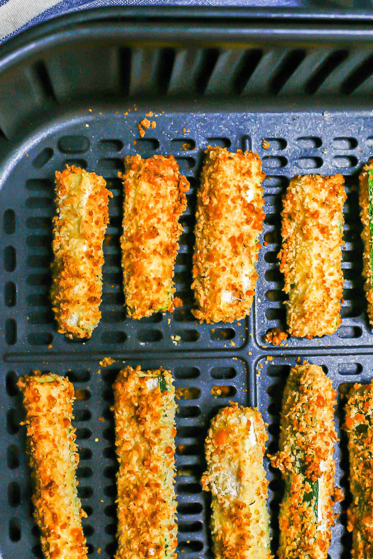 Close up of golden brown breaded zucchini sticks in an Air Fryer insert.