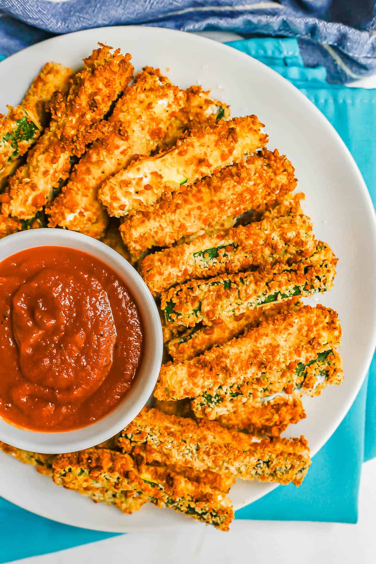 A plate of zucchini fries on a round white plate with a small bowl of marinara.