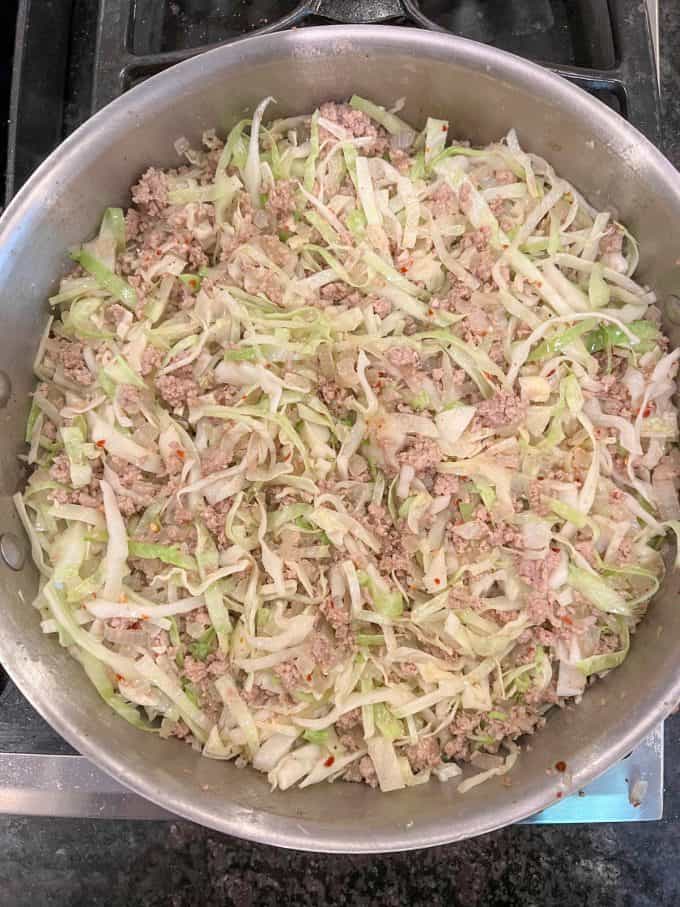 Cooked ground turkey with onions and wilted cabbage in a large deep skillet.