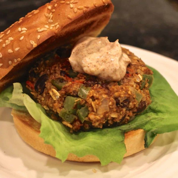 A black bean veggie burger served on a wheat bun with lettuce underneath and a spiced yogurt sauce on top.