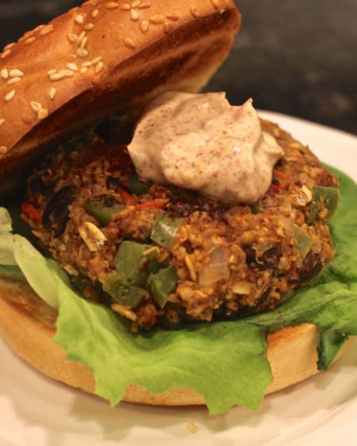 A black bean veggie burger served on a wheat bun with lettuce underneath and a spiced yogurt sauce on top.