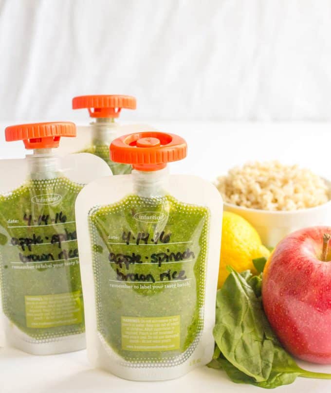 A trio of apple spinach brown rice squeezes in clear pouches with orange lids.