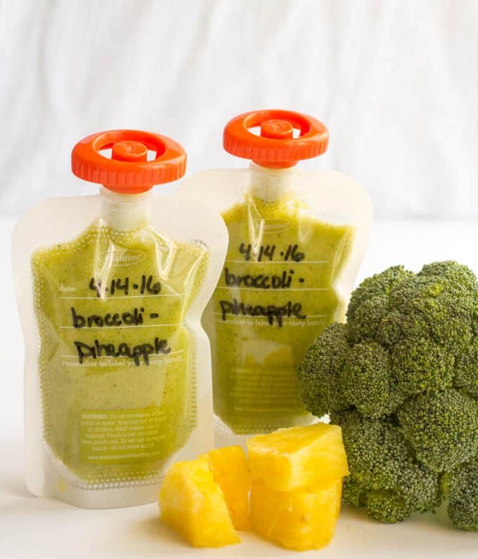 Two broccoli pineapple baby food squeezes in clear pouches with orange lids.