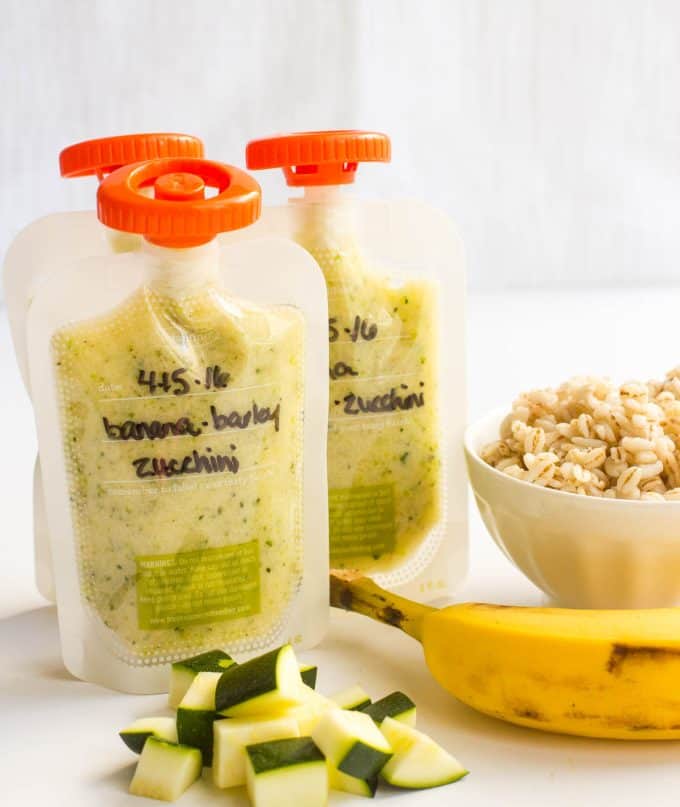 A trio of banana barley zucchini homemade squeezes in clear pouches with orange lids.