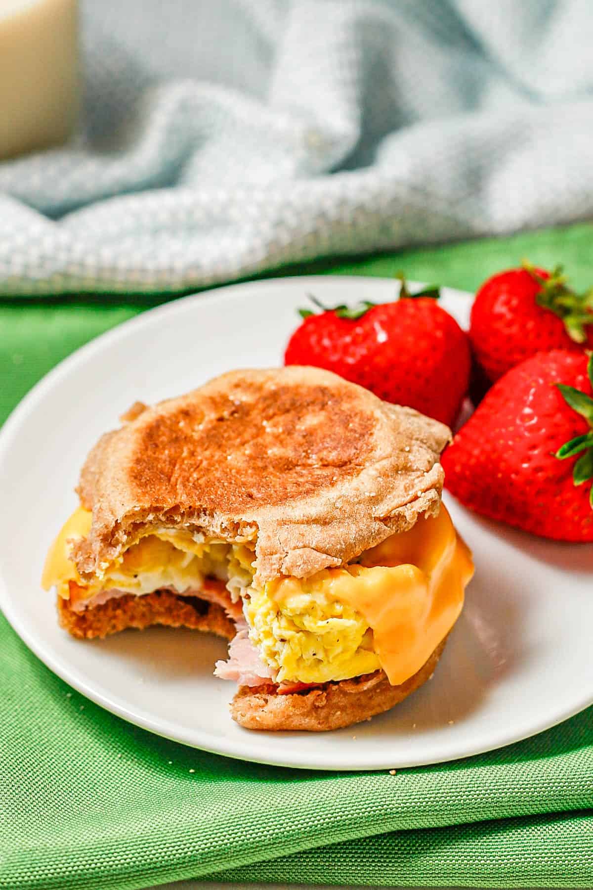 A homemade English muffin sandwich on a white plate with a bite taken out of it.