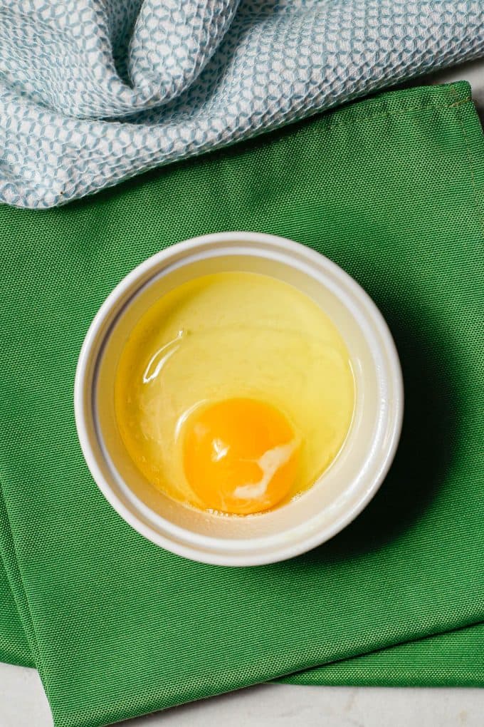 An egg cracked into a small white ramekin dish.