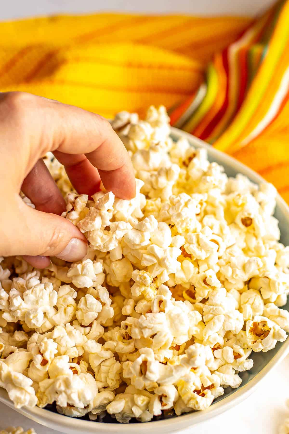 A hand picking up popcorn from a blue and white bowl.